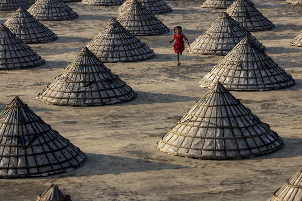 Children run amongst hundreds of traditional rice mills made from bamboo from Azim Khan Ronnie